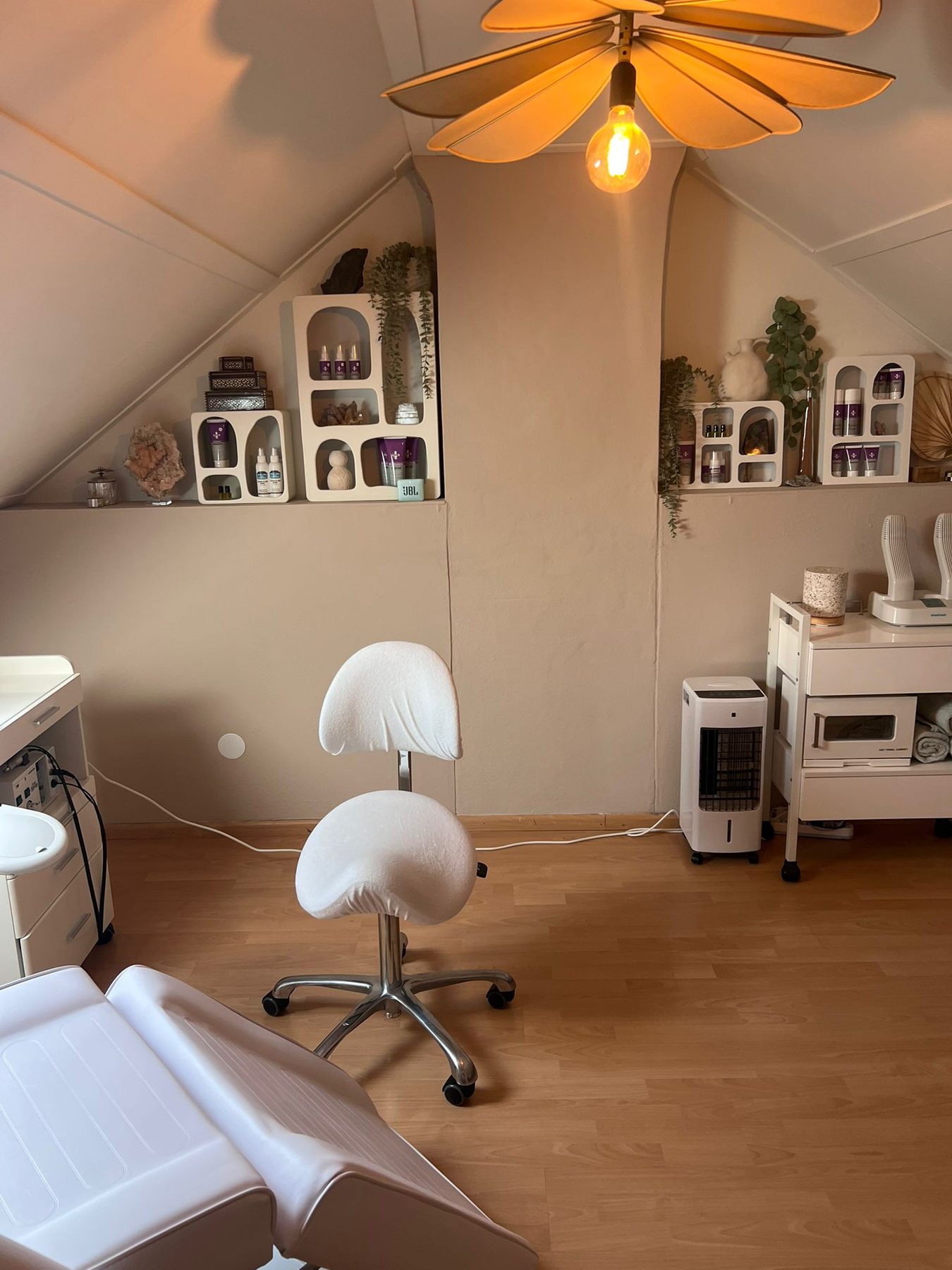 De behandelkamer met een zadelkruk, planken met verzorgingsproducten en een bloemvormige lamp